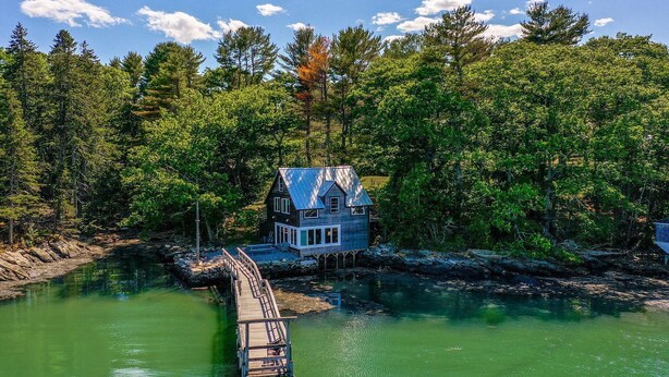 A house with a dock extending into a green body of water, surrounded by dense forest. - Historic Boathouse over Water, Stunning View, Private Pier + Dock + Mooring (Westport)
