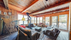 A cozy cabin interior with a wooden ceiling, large windows, a fireplace, and a sofa set. - Historic Boathouse over Water, Stunning View, Private Pier + Dock + Mooring (Westport)