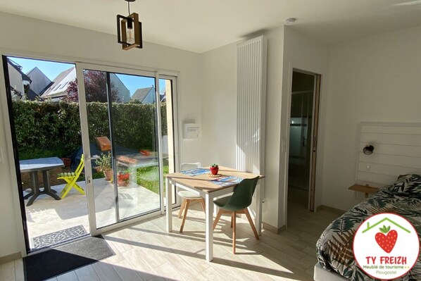 A modern room with a sliding glass door leading to a patio, a wooden table with chairs, and a bed with a patterned cover.