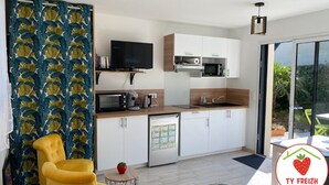Een moderne keuken met witte kasten, een magnetron en een koffiezetapparaat. Er staat een televisie op een houten plank, en een gele stoel is te zien.