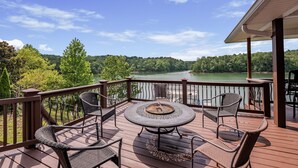 Une terrasse dotée d’une table ronde et de chaises, offrant une vue sur un lac et des collines boisées.