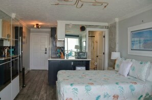 Quarto com cama, cozinha compacta, banheiro e vista para o mar.