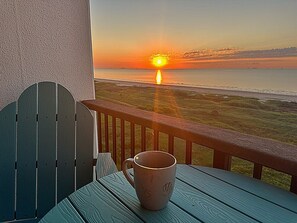 A wooden deck with a table and a mug, overlooking a sunset over the ocean.