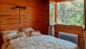 Une chambre dans un chalet en bois, avec un lit, des oreillers, une fenêtre et un radiateur.
