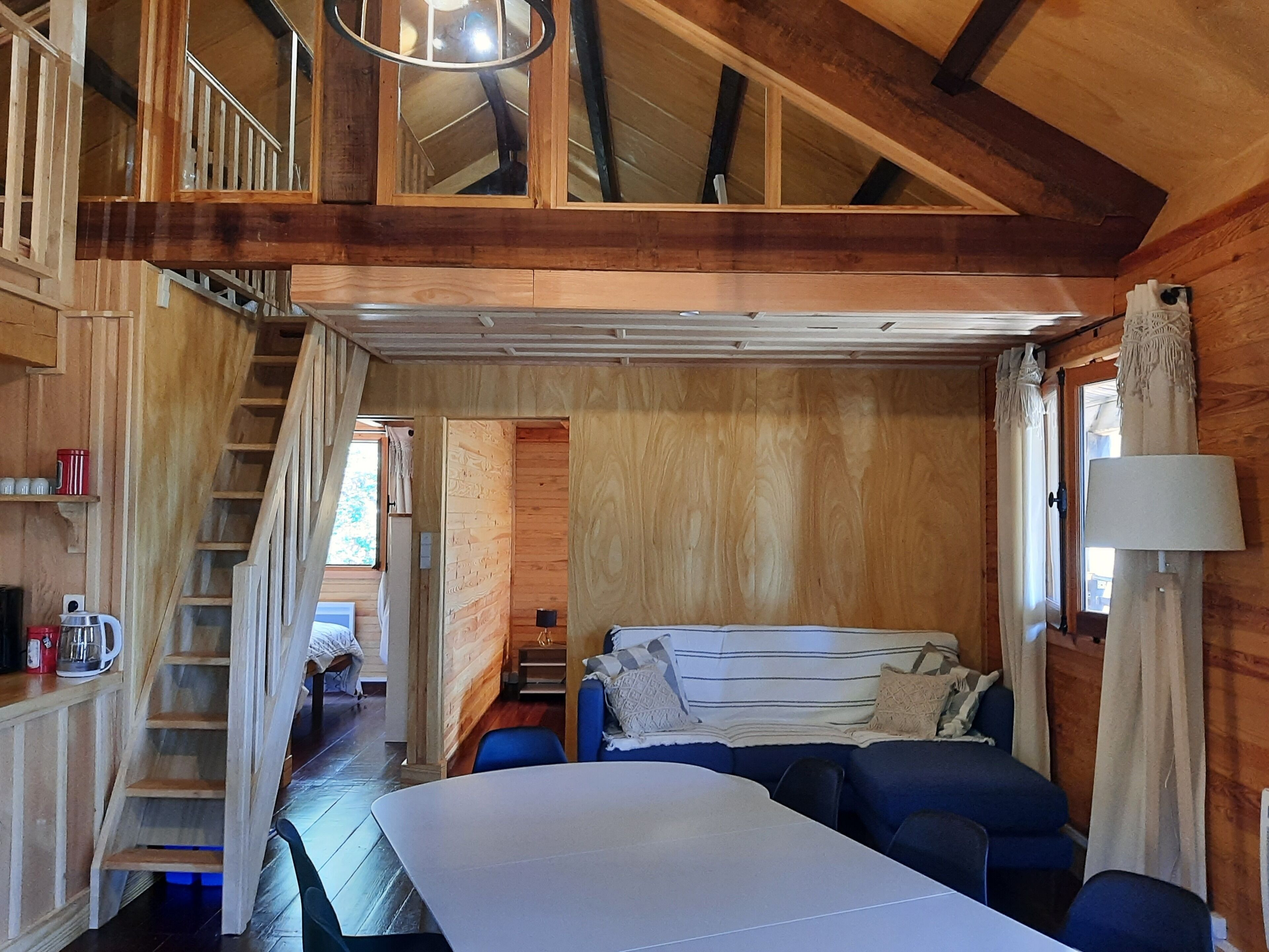 L’intérieur chaleureux d’un chalet avec un lit en mezzanine, une table à manger et un escalier menant à un deuxième niveau.