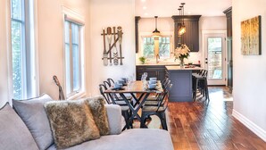 A modern kitchen with dark cabinetry, a central island, and a dining area with a wooden table and chairs. - Luxury stay at a Beach House • Sleeps 8 • Walk to Bay Beach (Crystal Beach)