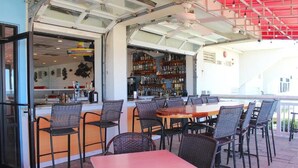 Un área de comedor al aire libre con una barra, sillas de mimbre y una mesa roja.
