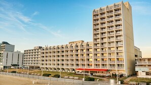 Un hotel de varios pisos con balcones, un espacio de estar techado al aire libre y vista al mar.
