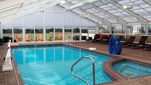 Una piscina interior con paredes de vidrio transparente, sillones de descanso y una zona de estar cubierta.