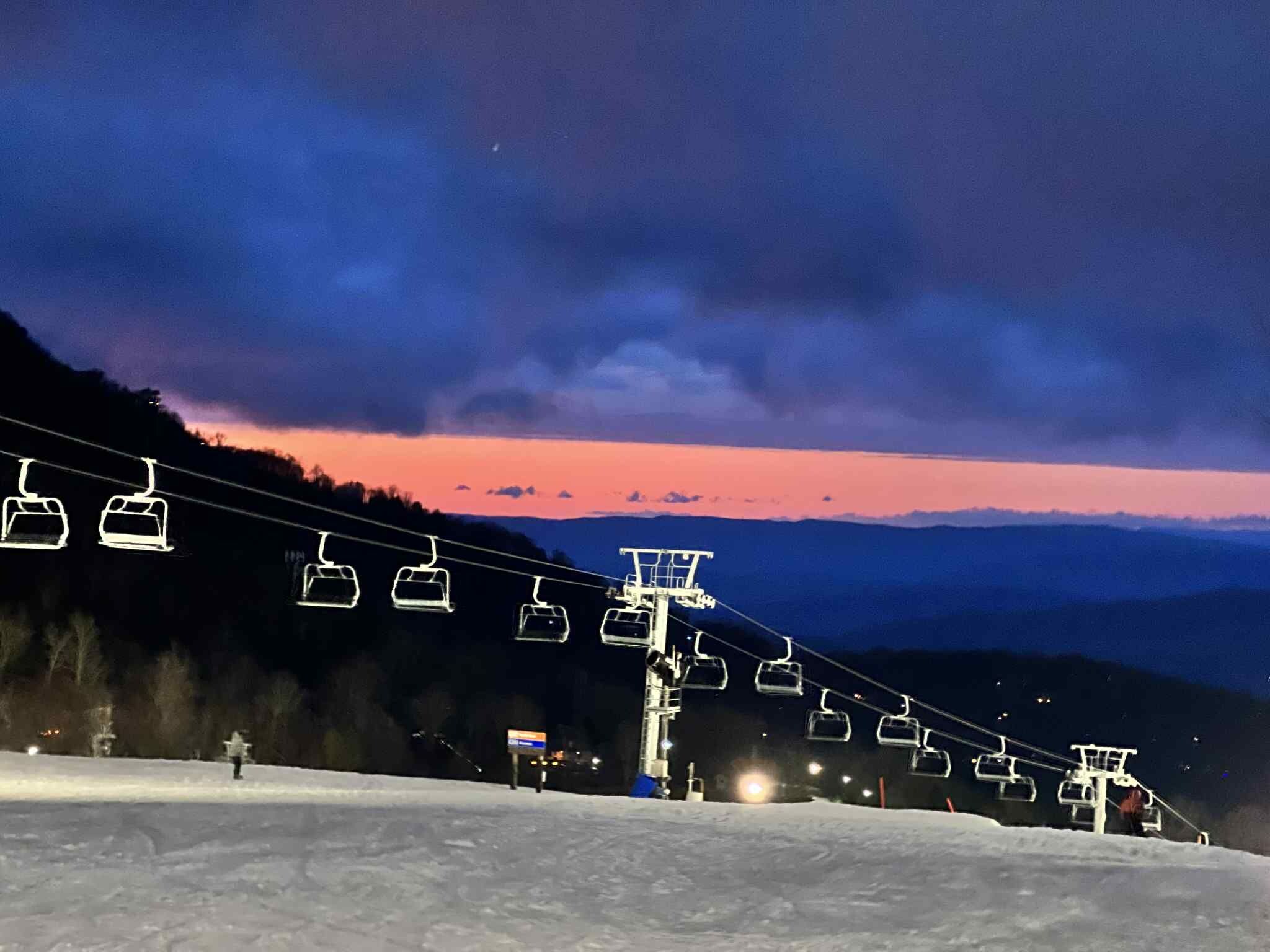 A ski lift at dusk with a mountain backdrop.