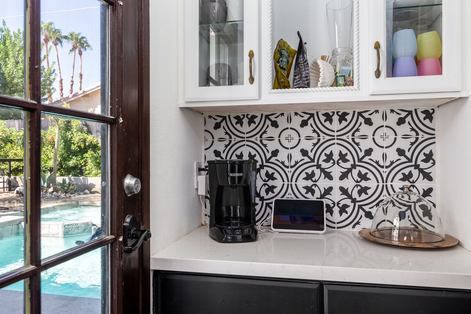Een keuken met een koffiezetapparaat, een tablet en een glazen kast met decoratieve spullen.