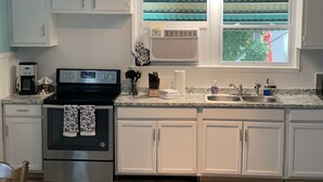 A kitchen with white cabinets, a stove, a coffee maker, and a window with curtains. - Rustic Ocean View Beach House - BEST Location in Ocean View! 2 bed/1 bath House (Norfolk)