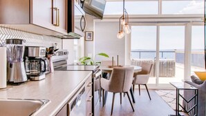 Une cuisine moderne dotée d’un grand îlot central, d’appareils électroménagers en acier inoxydable et d’un coin repas offrant une vue sur l’océan.