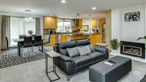 Ein modernes Wohnzimmer mit einer Couch, einem Essbereich mit Stühlen, einer Küche mit Holzschränken und einem Kamin.