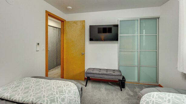 Ein Hotelzimmer mit einem Bett, einer kleinen Bank, einem an der Wand montierten Fernseher und einer Schiebetür aus Glas.
