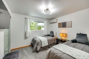 A hotel room with two beds, a desk with a lamp, an air conditioner, and a window with curtains. - Redmond Retreat w/ Fenced Yard & EV Charger (Redmond)