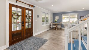 A spacious entryway with a wooden door, a dining area with a table and chairs, and a staircase with white railings.