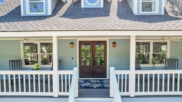 A two-story house with a front porch, a double door with glass panels, and a small staircase leading up to the entrance.