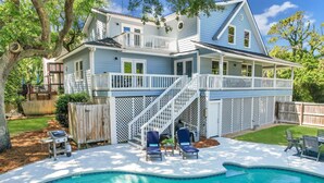 A two-story house with a swimming pool, outdoor seating, and a wooden deck.