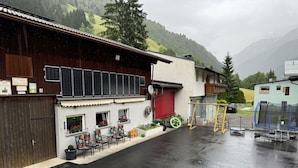 Un bâtiment doté d’une façade en bois, d’une porte de garage rouge et d’un petit espace extérieur aménagé avec des chaises et des tables.