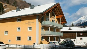 Un immeuble à plusieurs étages, dont le toit est recouvert de neige, doté de balcons et d’une enseigne indiquant « Apart Sesselebenhof Sauna ».
