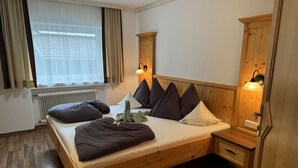 Una cama de madera con cabecera, lámparas de noche, un radiador y una ventana con cortinas.
