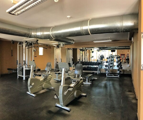 Une salle de sport équipée de divers appareils d’exercice, notamment des tapis de course, des appareils de musculation et des haltères.