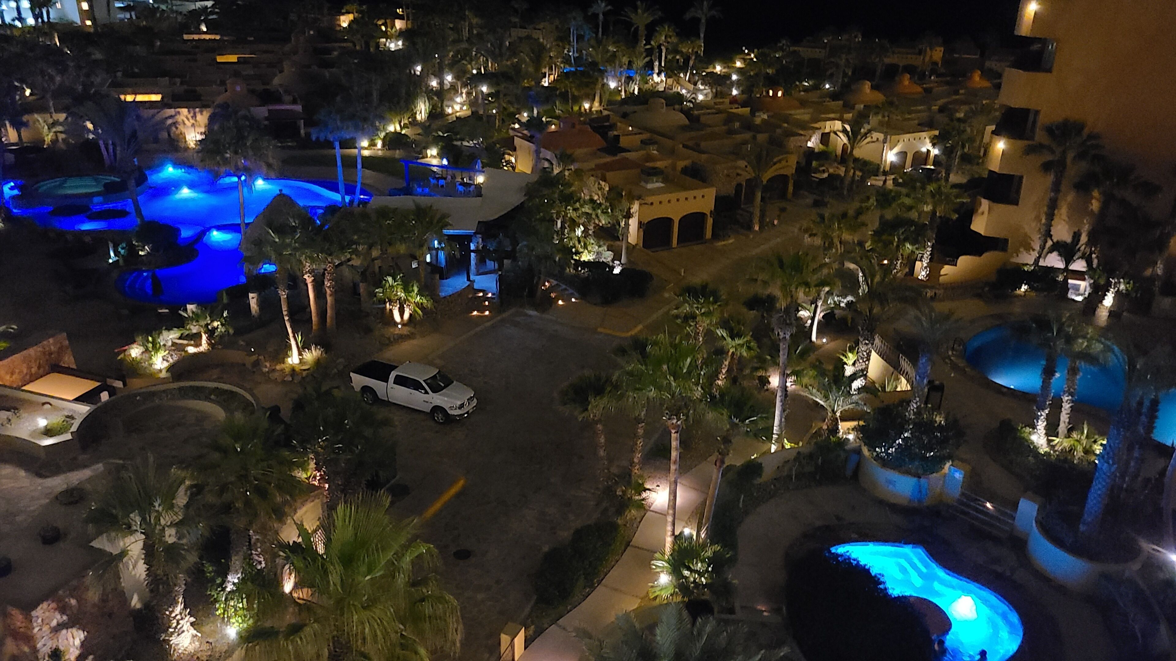 Un resort con varias piscinas, palmeras y un vehículo blanco estacionado en la entrada.