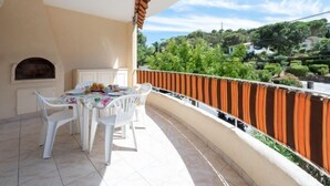 Ein Balkon mit Tisch und Stühlen, gefliestem Boden und Blick auf eine Hügellandschaft mit Grünflächen und Gebäuden.