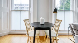 Ein Essbereich mit einem runden Tisch, zwei Holzstühlen, einer weißen Vase und einer Stehlampe.