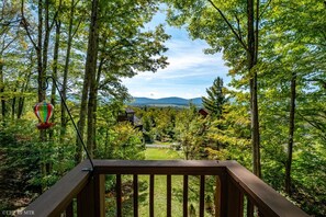 Une terrasse en bois offrant une vue sur une zone boisée et sur des montagnes lointaines.