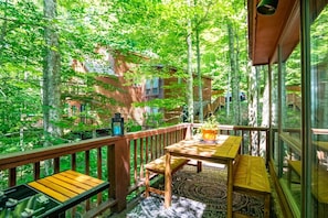 Un terrazzo in legno con tavolo e sedie, circondato da alberi e vista su un edificio.
