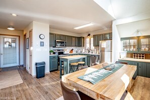 Uma cozinha moderna com ilha central, eletrodomésticos embutidos e área de refeições com mesa e cadeiras de madeira.