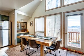 A kitchen with a dining area, a refrigerator, and a view of a snowy landscape through large windows. - Trail Magic - 57 Mountain Laurel Lane (Davis)