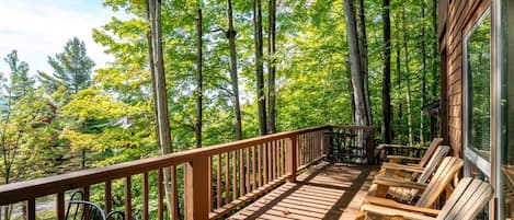 Une terrasse en bois avec une rambarde, des sièges d’extérieur et une vue sur une forêt.