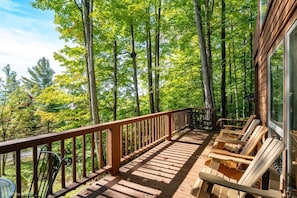 A wooden deck with a railing, outdoor seating, and a view of a forest.