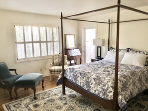 Classic four-poster bed with a floral-patterned bedspread, complemented by a wooden chair and a small table with a lamp.
