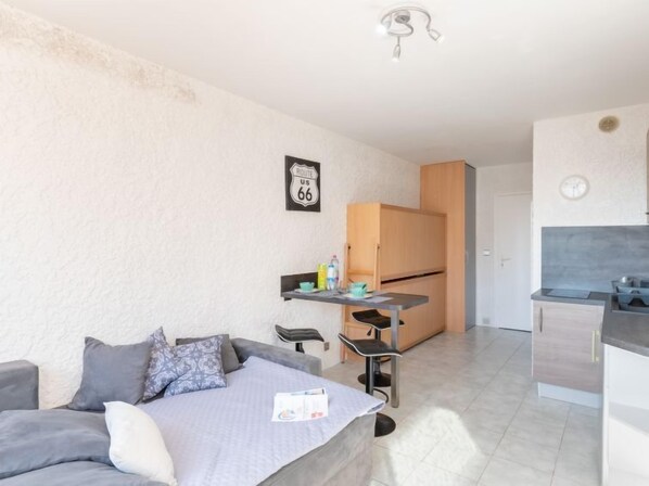 Ett kompakt bostadsutrymme med ett litet kök, en matplats och en soffa med kuddar.