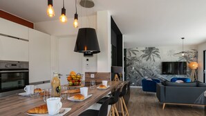 Ett modernt kök med en köksö i trä, barstolar och en matplats med tv och sittplatser.