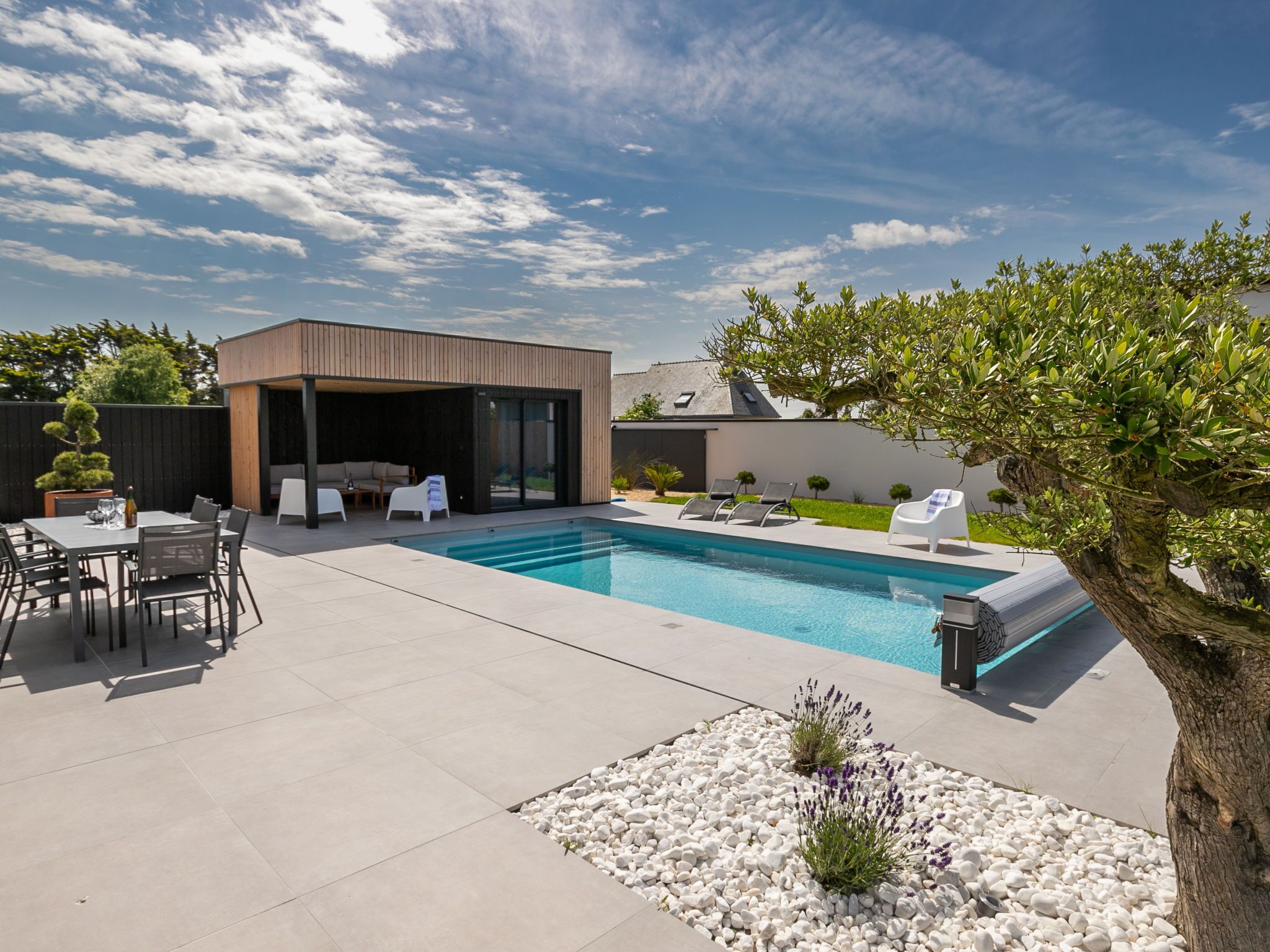 Uma área moderna de piscina externa com espaço coberto para relaxar, espreguiçadeiras e área de refeições.