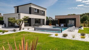 Ett modernt hus i två våningar med en swimmingpool, utomhusmöbler och en välskött trädgård.