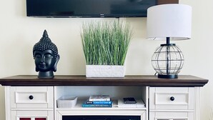 Een witte entertainmentkast met een flatscreen-tv erboven, een Boeddha-beeldje, een potplant, een lamp en een open haard.