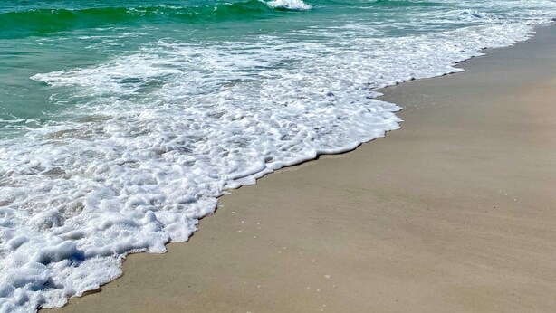 Een strand met golven die zachtjes op het strand ruisen onder een heldere lucht.
