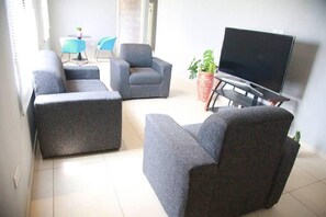 A living room with grey sofas, a TV, and a small table with chairs. - Captivating 2-Bed Ensuite Apartment in Accra (accra)