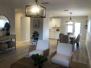A modern living room with a dining area, featuring a large chandelier, wicker furniture, and a potted plant. - Newly Renovated Casita West Little Havana (Miami)