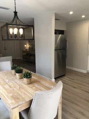 A modern kitchen with a stainless steel refrigerator, a wooden dining table with three potted plants, and a pendant light fixture above. - Newly Renovated Casita West Little Havana (Miami)