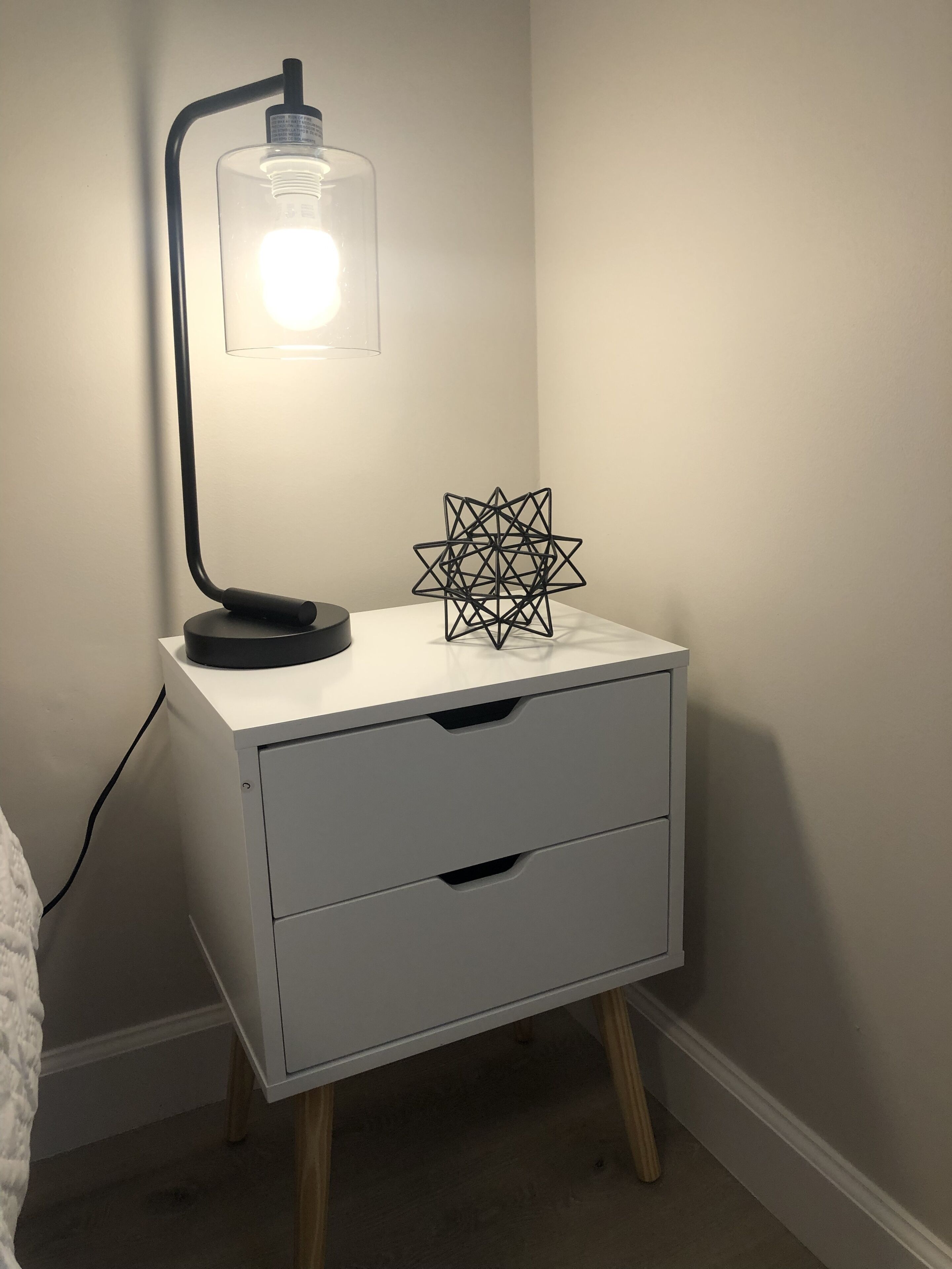 Una mesita de noche con una lámpara y un objeto decorativo geométrico.