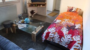 A modern living room with a sofa, a coffee table, a TV, and a bed with a colorful bedspread.