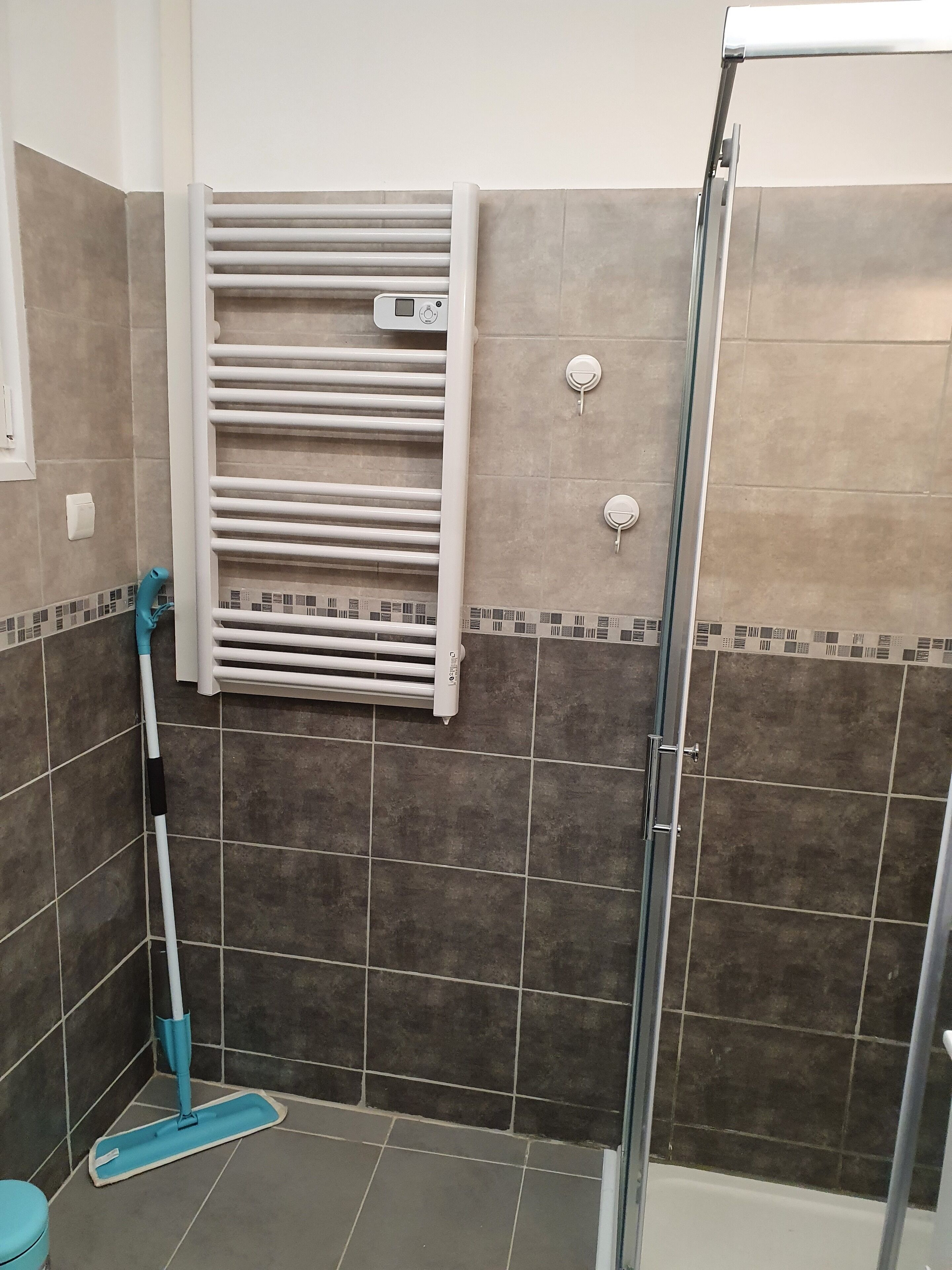 Ein Badezimmer mit Dusche, einem weißen Handtuchhalter und einem Mopp, der an der Wand lehnt.