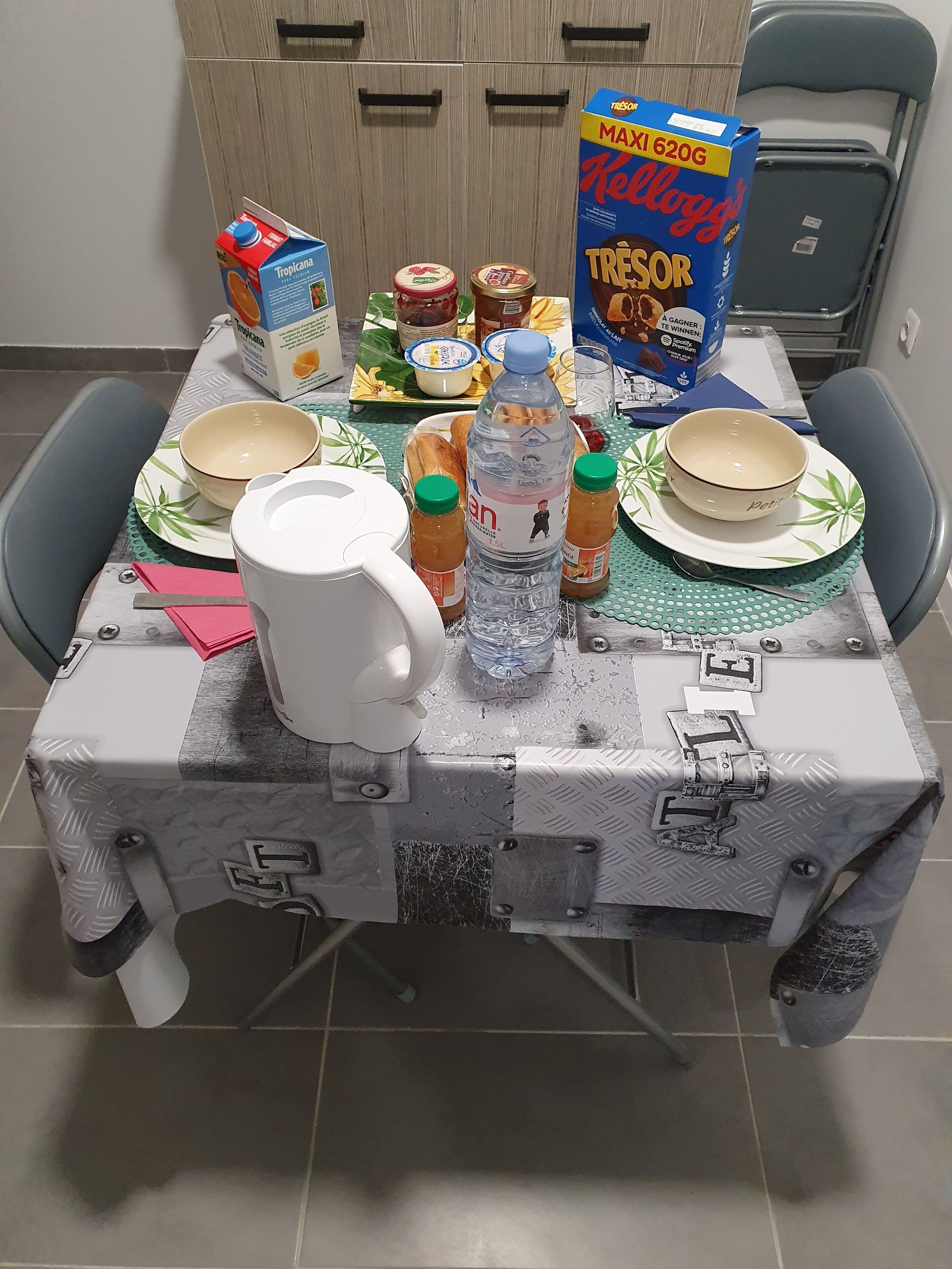 Een eettafel gedekt met borden, kommen, een fles en een doos ontbijtgranen.